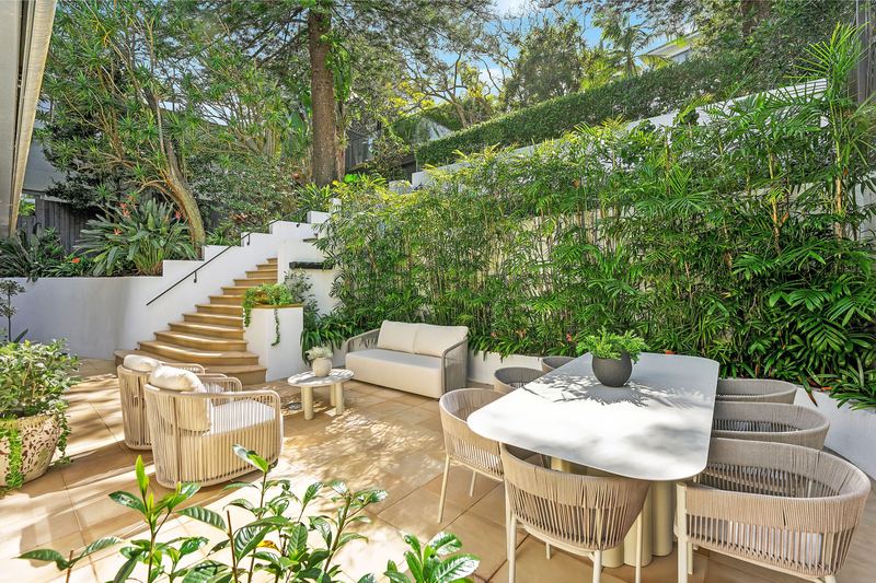 Paved alfresco terrace with outdoor lounge and dining settings, screened by bamboo, with stairs up to the lawn