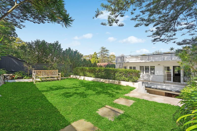 Level green lawn with a timber bench and hedges, the rear of the house and its rooftop terrace beyond