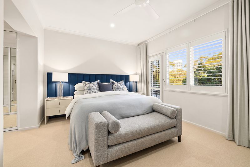 Main bedroom with navy upholstered bedhead, French doors to a balcony and treetop views